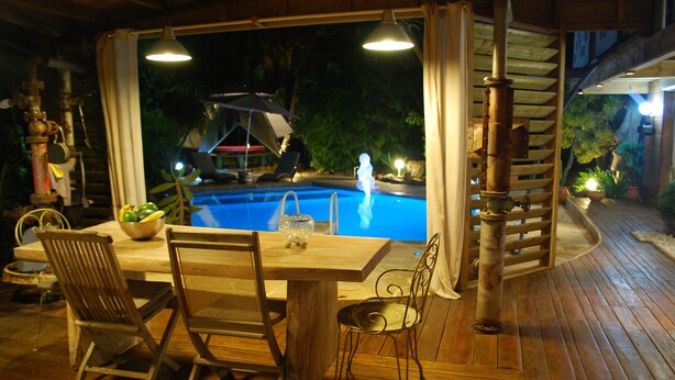 An outdoor pool area with a wooden deck, a table with chairs, and a view of the pool at night. - Luxury villa with pool on an ancient sugarcane plantation (LAMENTIN)
