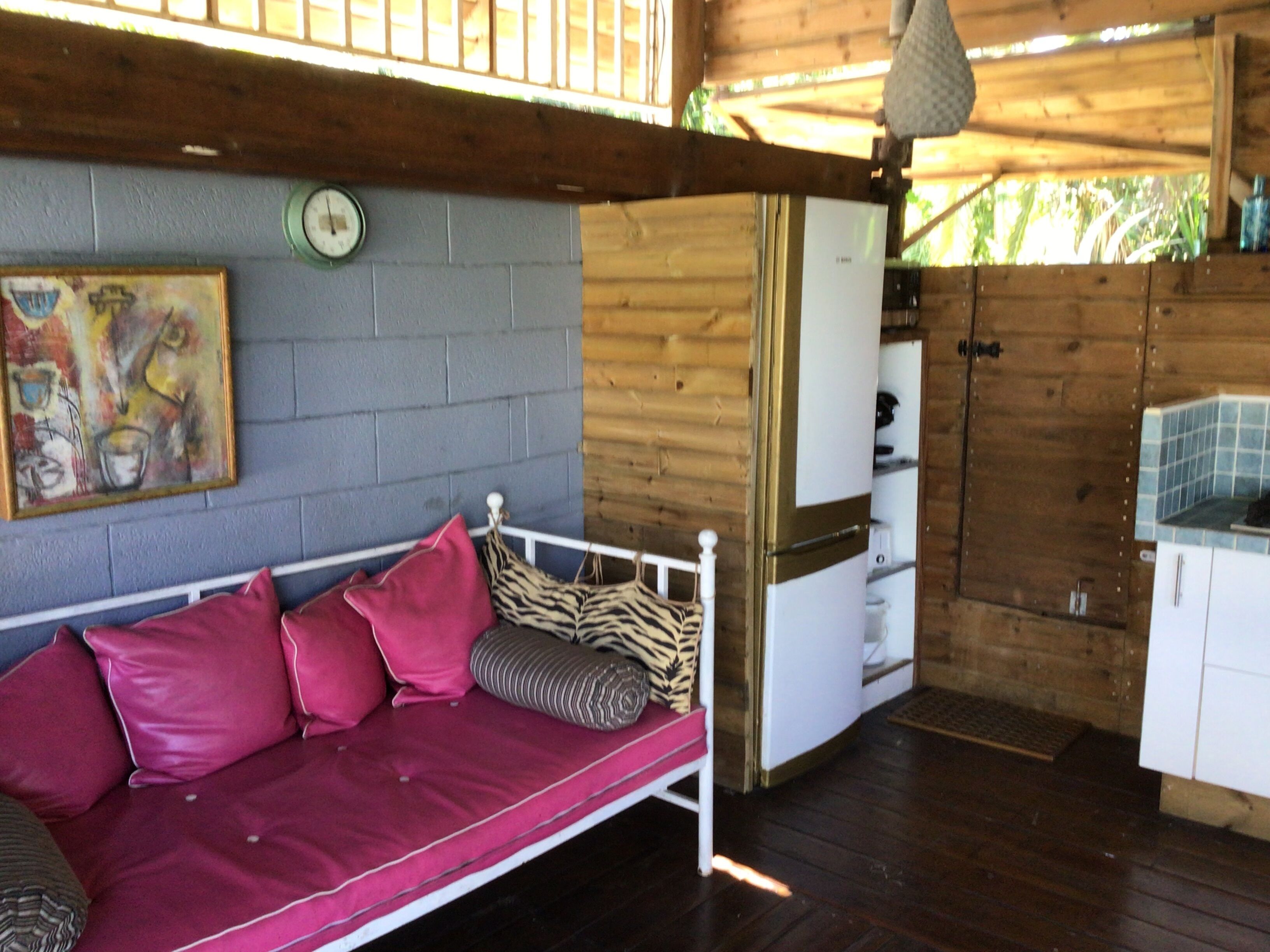 Interior de una cabaña de madera con una cama, una zona de cocina y un reloj de pared.