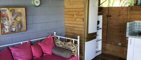 Interior de una cabaña de madera con una cama, una zona de cocina y un reloj de pared.