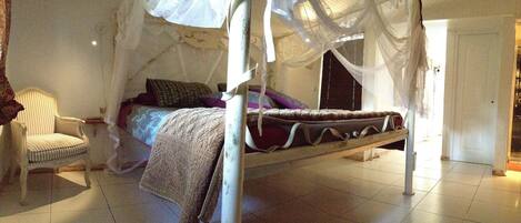 A four-poster canopy bed with a white canopy, a striped armchair, and a bedside table.