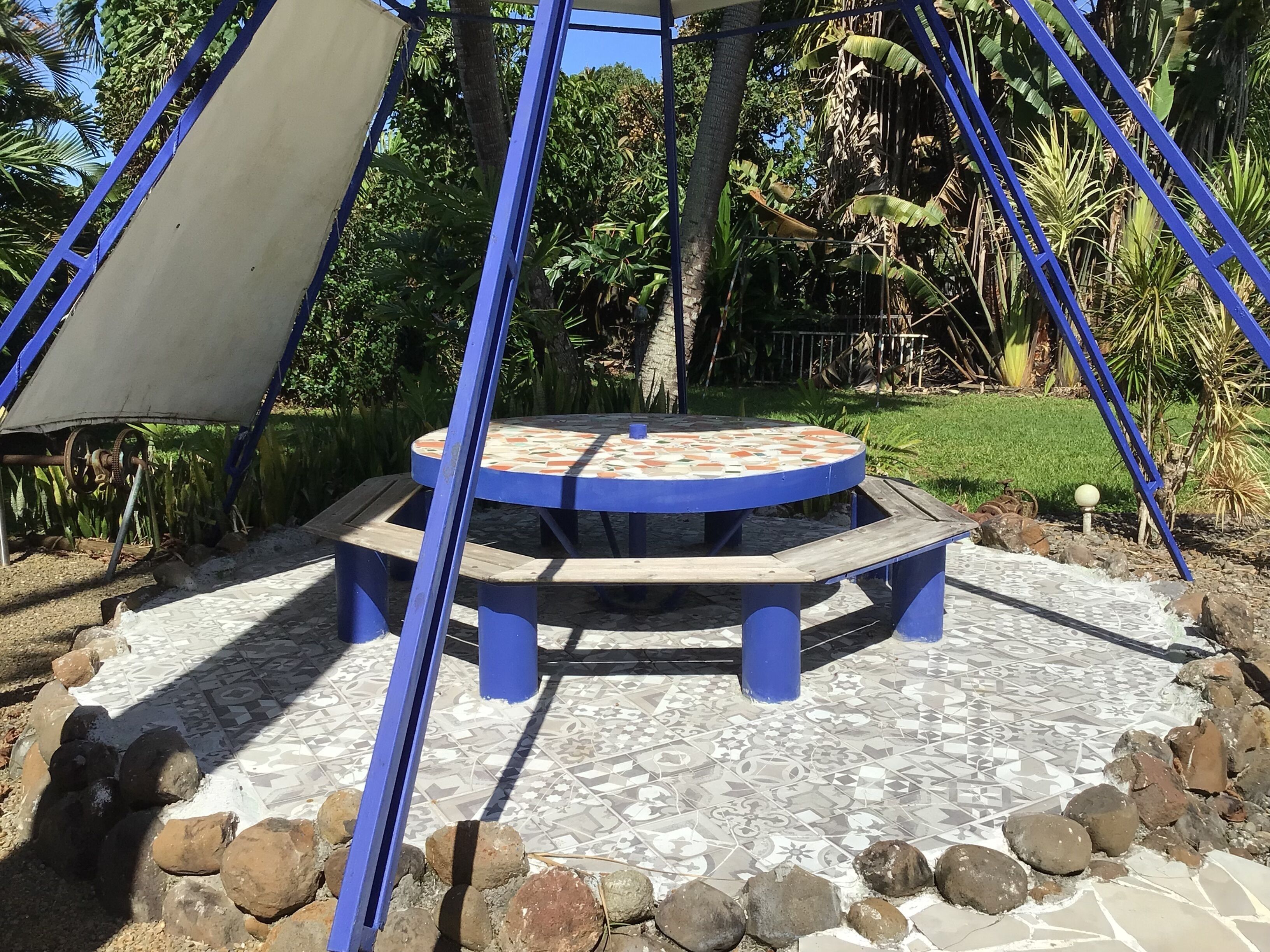 Un espacio de estar al aire libre circular con suelo estampado, rodeado de rocas y sostenido por postes de metal azules.