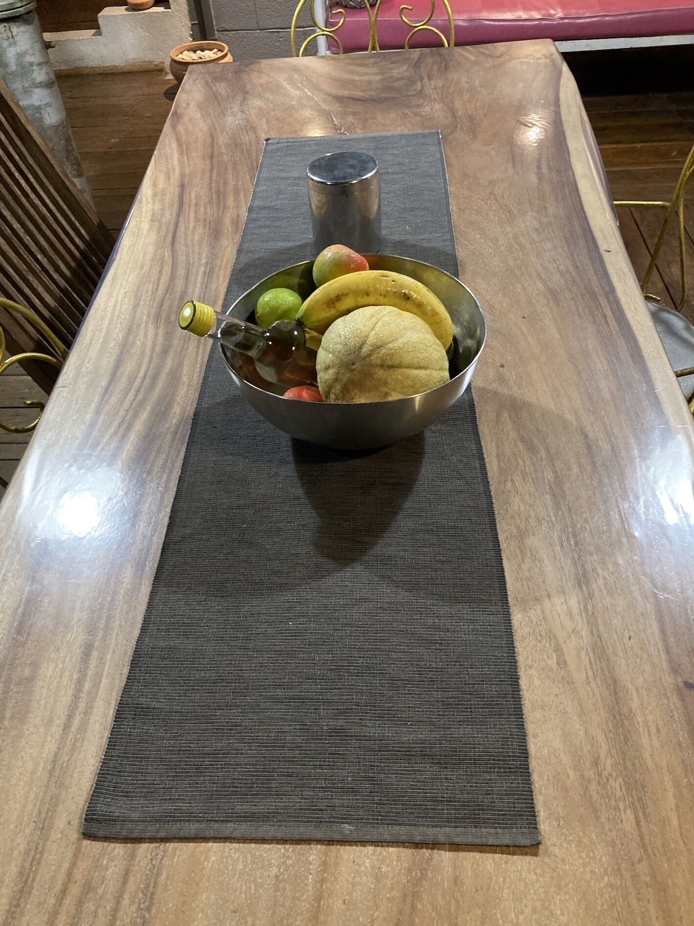 A wooden table with a metal bowl containing fruits and a bottle.
