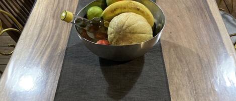 A wooden table with a metal bowl containing fruits and a bottle.