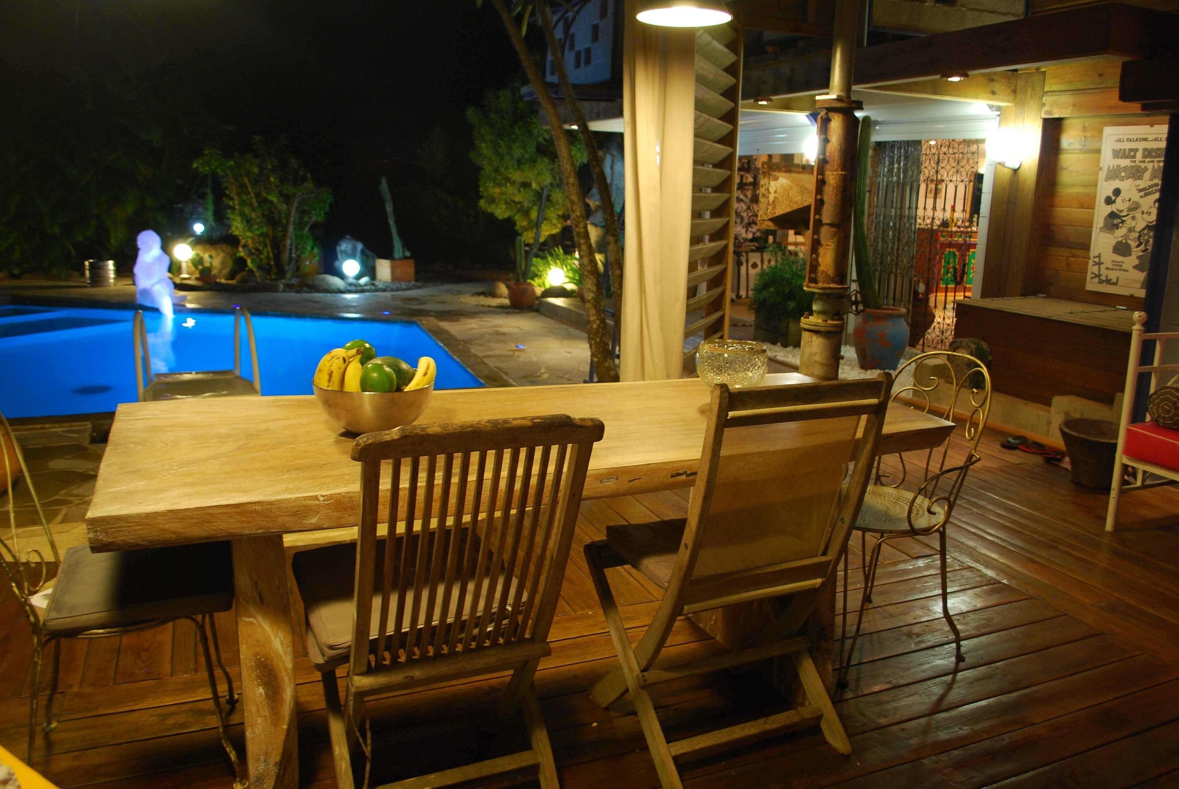 Um deck de madeira com mesa de bilhar, cadeiras e uma tigela de frutas.