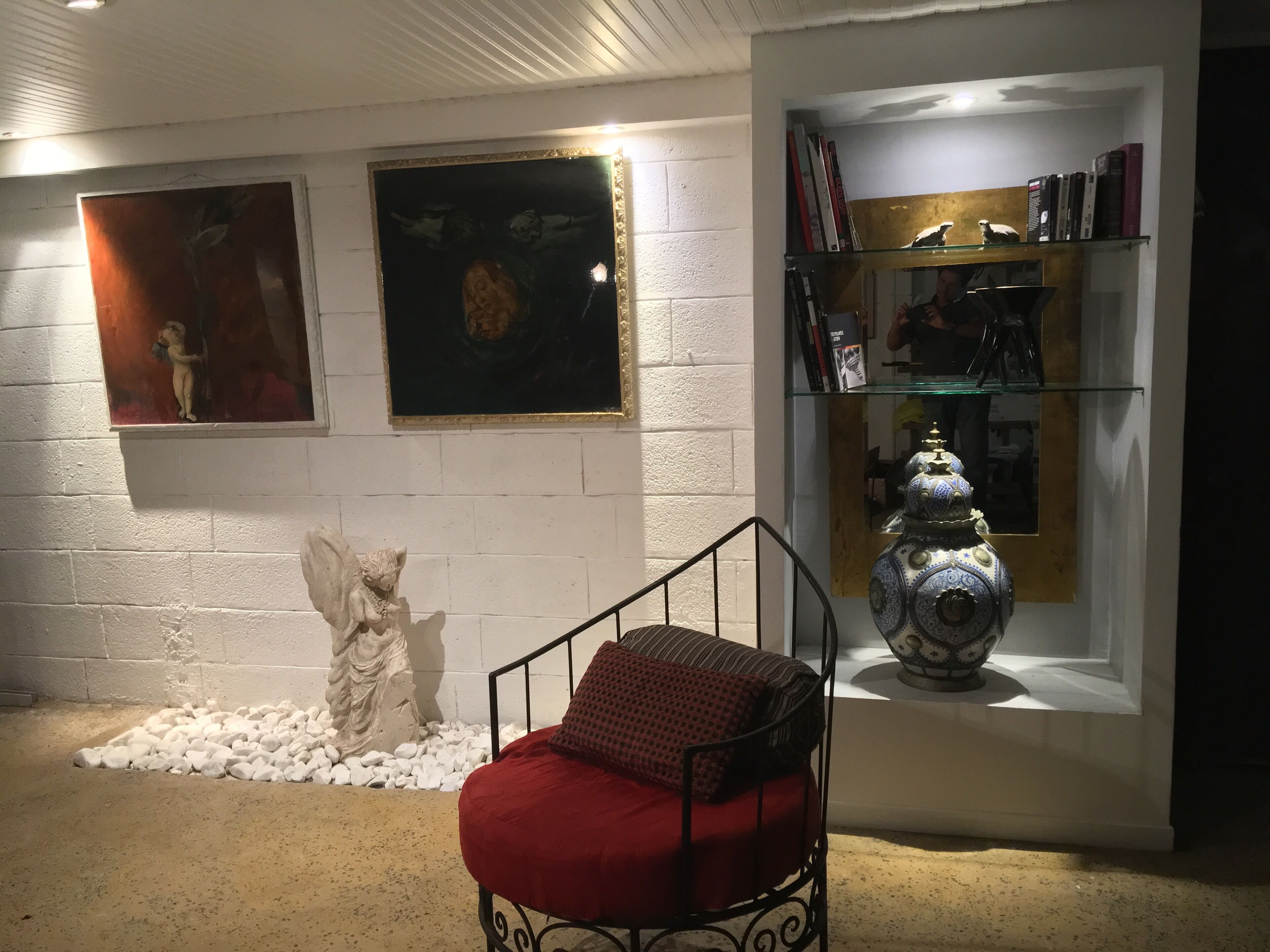 A room with a bed, a sculpture, and a bookshelf with books and decorative items.