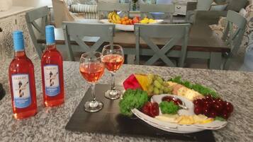 A dining table with a fruit platter, two bottles of red wine, and three wine glasses.