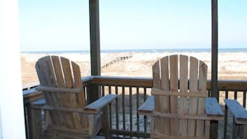 A wooden deck with two Adirondack chairs facing a beach.