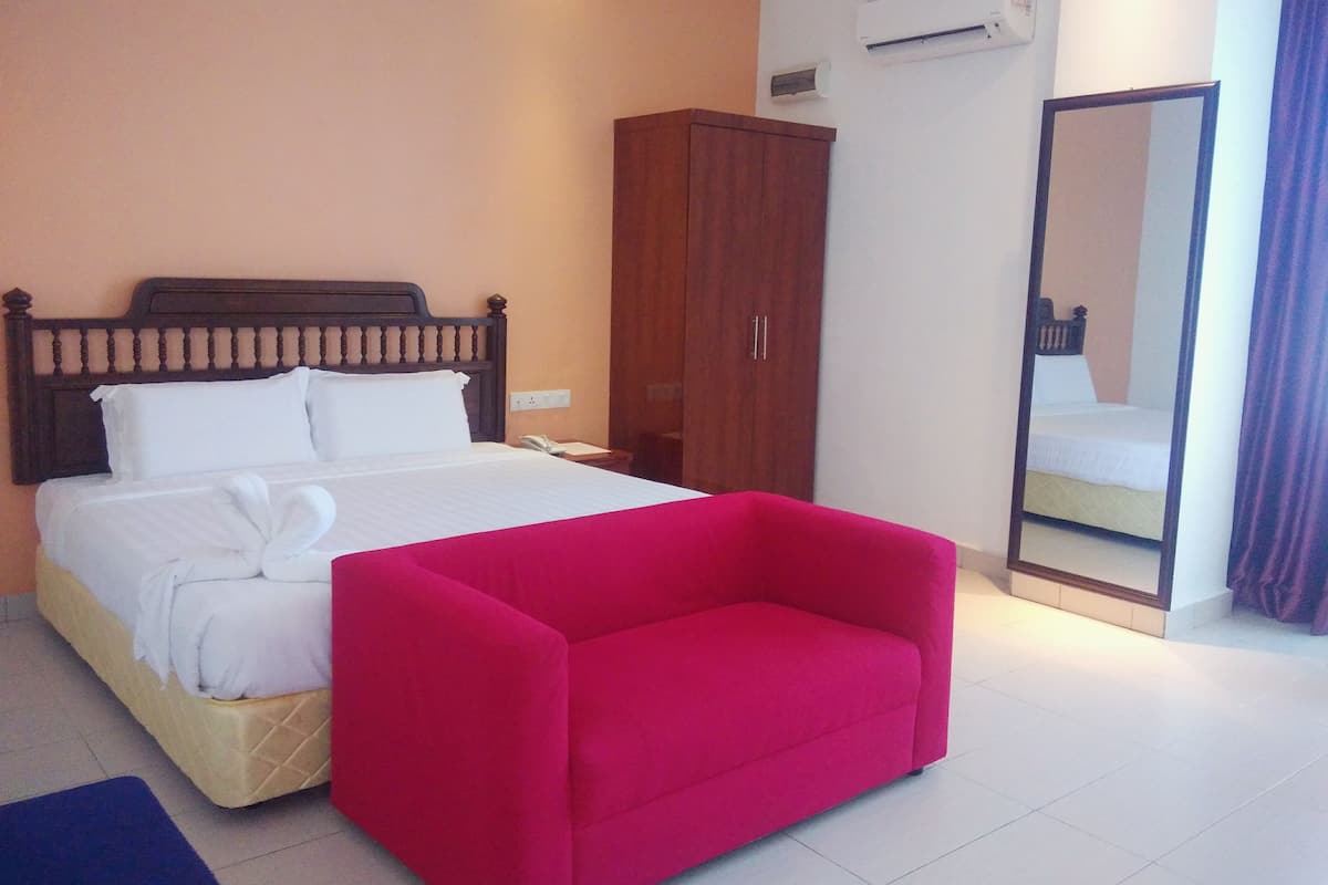 A hotel room with a bed, a wardrobe, a mirror, and a red chair.