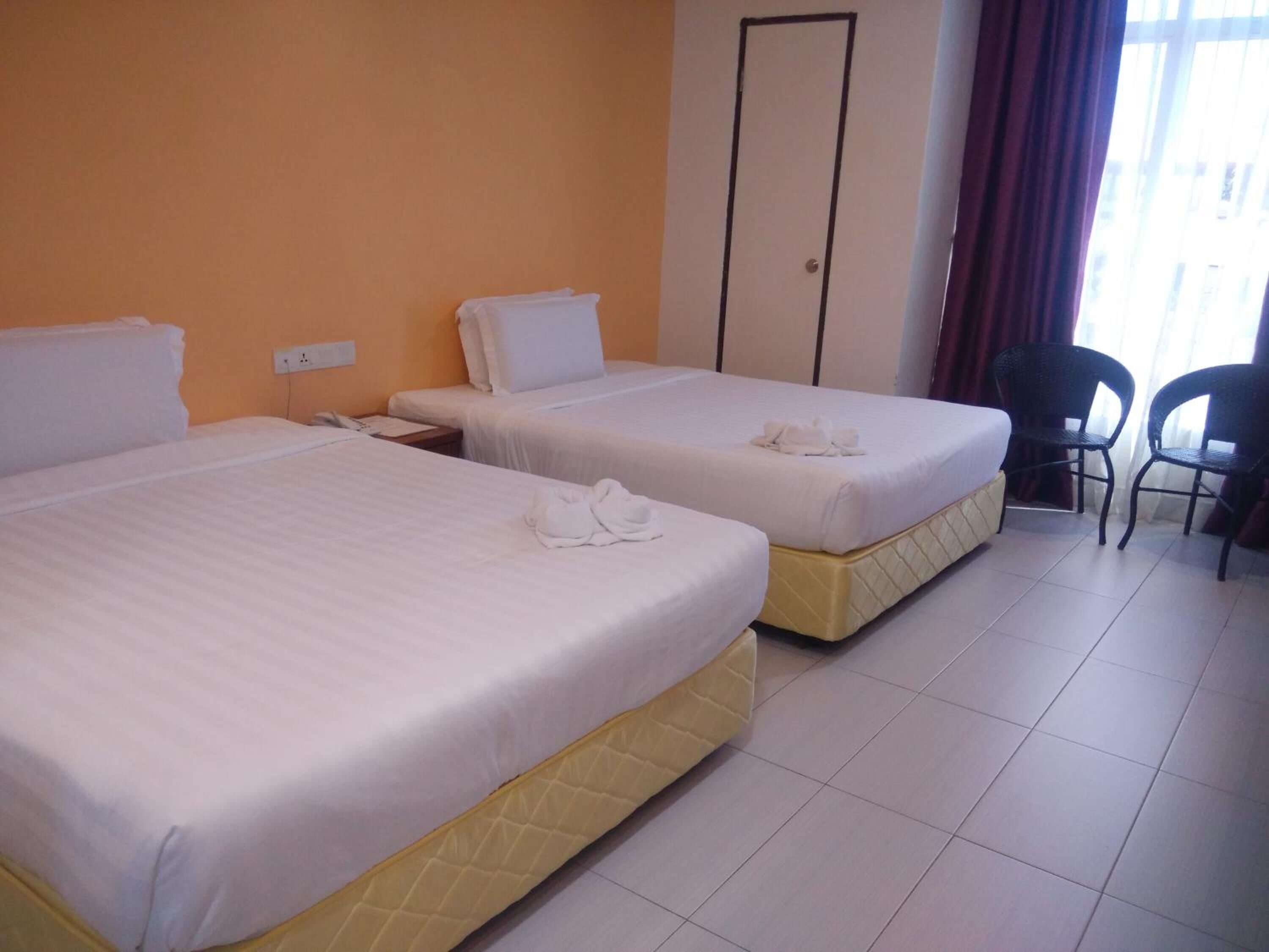 A hotel room with two beds, a desk, a chair, and a door.