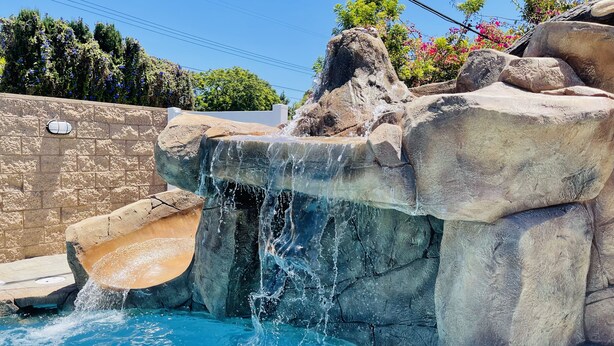 A pool with a waterfall feature surrounded by large rocks and a stone wall. - ULTIMATE PRIVATE WATER PARK & POOL Next Disneyland (Anaheim)