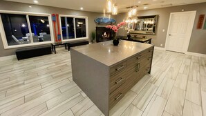 A modern kitchen with a large island, pendant lighting, and a view of the outside through large windows. - ULTIMATE PRIVATE WATER PARK & POOL Next Disneyland (Anaheim)