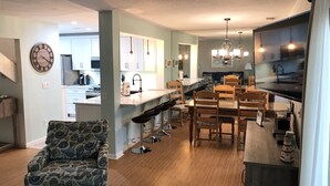 A modern kitchen with a dining area, wooden chairs, a bar stool, and a patterned sofa. - Sea & Tee Time - Plantation Club Villa  * REMODELED KITCHEN & ALL BATHS (Hilton Head Island)