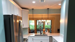 A modern kitchen with white cabinets, a stainless steel refrigerator, and a large window providing a view of greenery outside. - Sea & Tee Time - Plantation Club Villa  * REMODELED KITCHEN & ALL BATHS (Hilton Head Island)