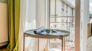 A room with a balcony, a table with a magazine and sunglasses, and a view of buildings outside. - Conte Rosso Apartments ARCA (Mestre)