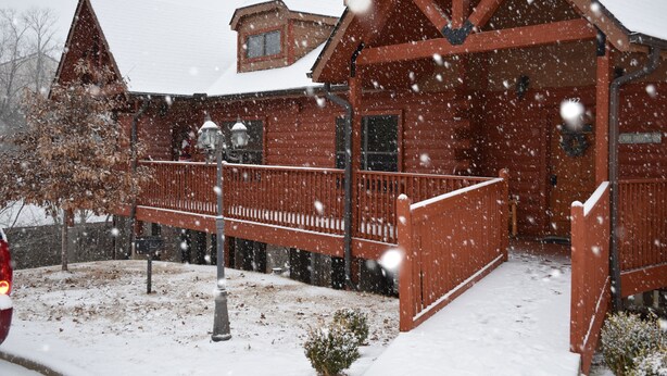 Uma cabana de madeira com varanda coberta de neve e um pequeno jardim.