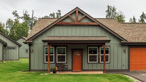 A two-story house with a green exterior, a brown front door, and a garage door. - Stoneridge Place Cottage #2 - Vacation or Executive Retreat 2BR 2BA Garage! (Wasilla)
