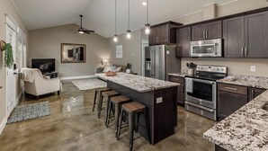 A modern kitchen with dark cabinets, stainless steel appliances, and a central island with bar stools. - Stoneridge Place Cottage #2 - Vacation or Executive Retreat 2BR 2BA Garage! (Wasilla)