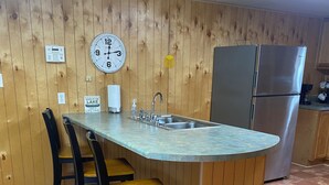 Una cocina con pared de madera, refrigerador de acero inoxidable, un lavamanos y un reloj.