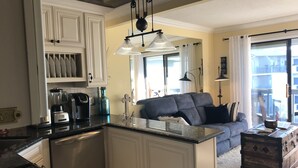 A modern kitchen with white cabinetry, a built-in island, and a dining area with a gray sofa and a wooden chest. - ABSOLUTELY AMAZING VIEW! (Tybee Island)