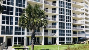 Een hotel met meerdere verdiepingen, balkons, een palmboom en een gazon.