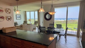 Een ruime keuken met een groot eiland, een eethoek met stoelen en uitzicht op het strand door grote ramen.