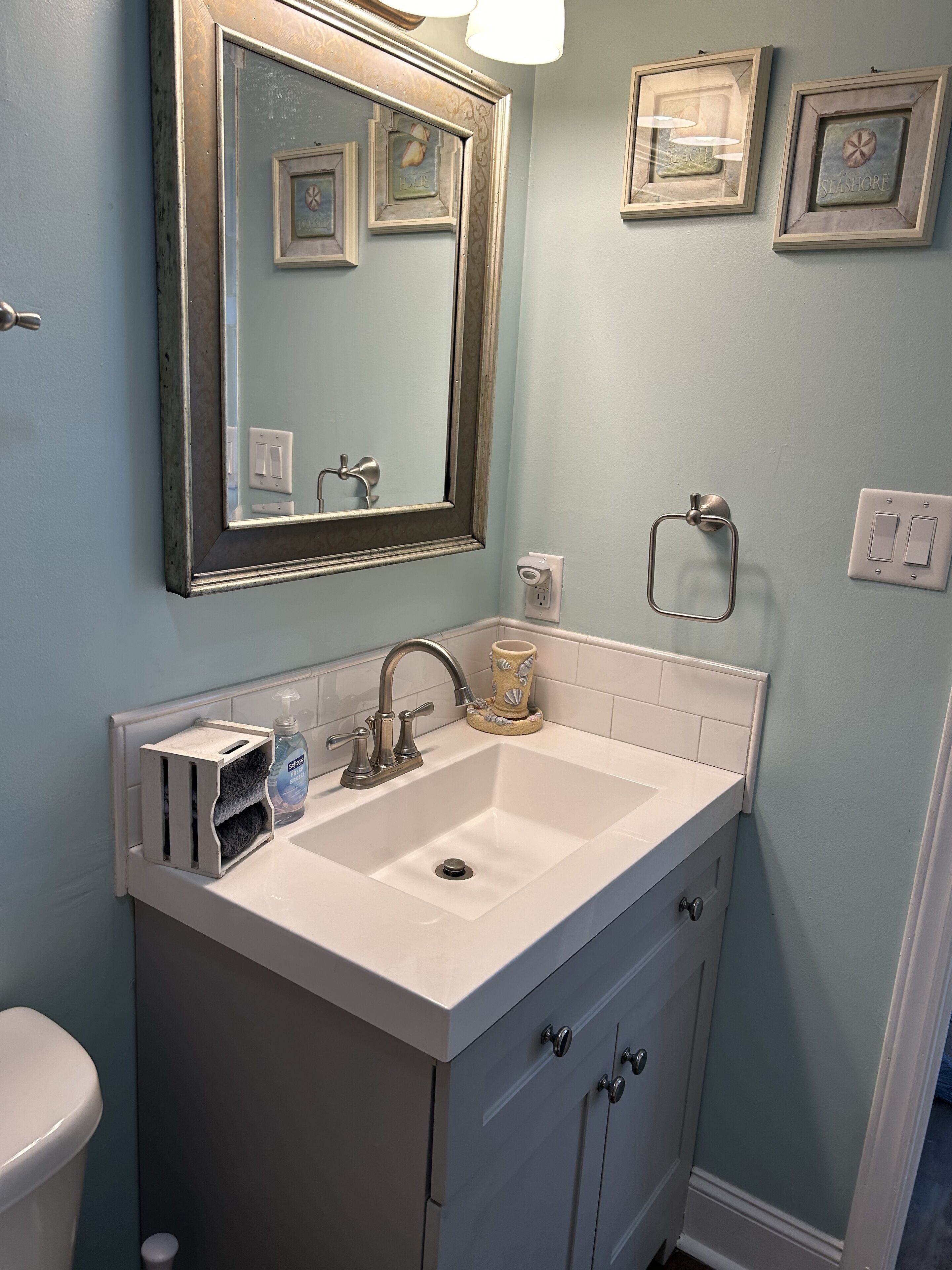 A bathroom with a white sink, a mirror, and a toilet. There are framed pictures on the wall and a towel rack.