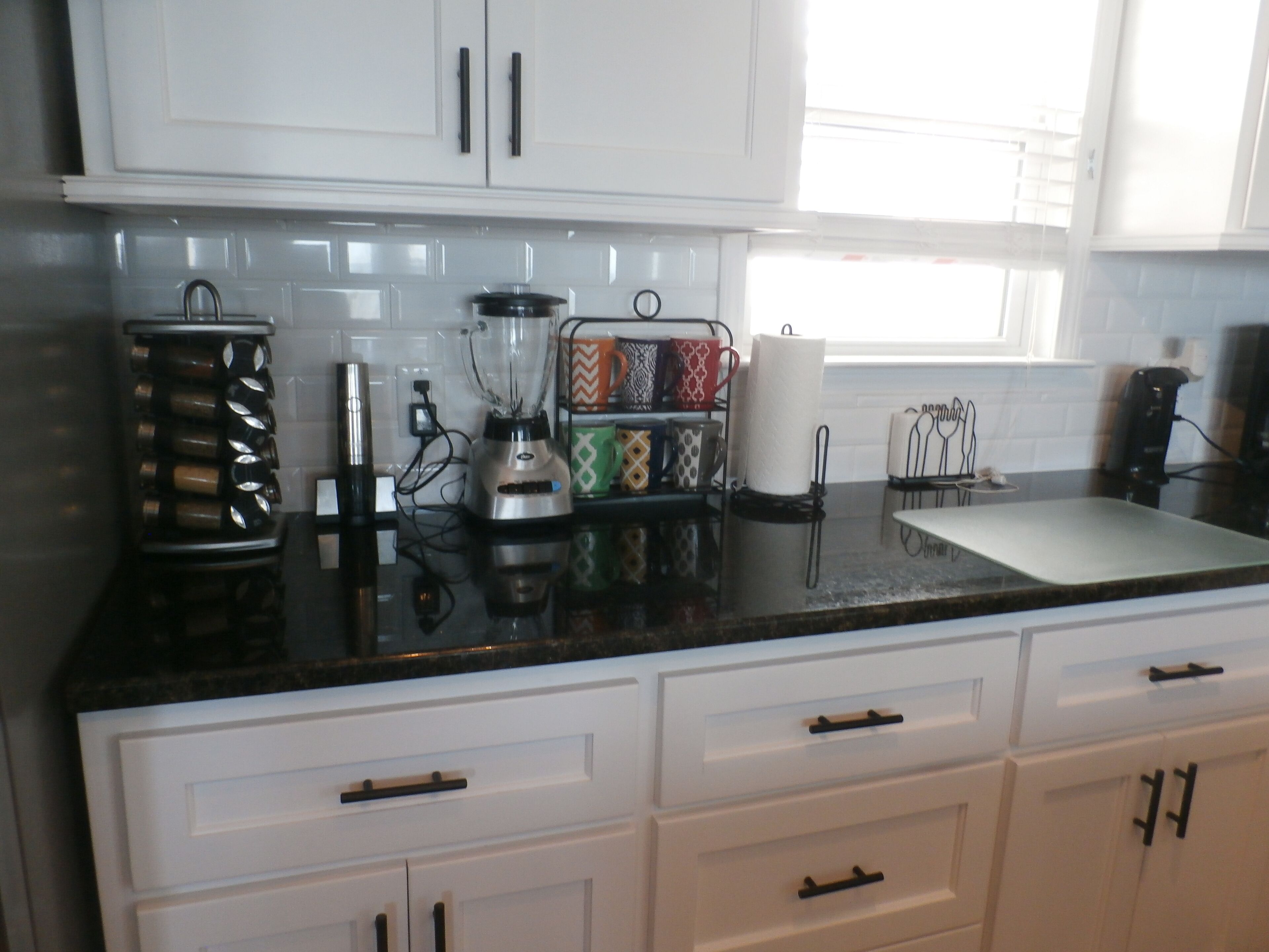A kitchen with white cabinets, a black countertop, and a window.