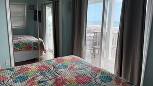 A bedroom with a large bed, a smaller bed, and a balcony with a view of the beach. -  Ocean Lakes / Oceanfront /   5 bed/ water park /slps 14 (myrtle beach)