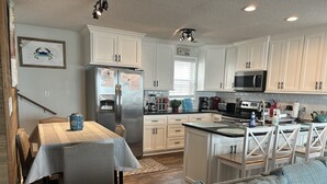 A modern kitchen with white cabinets, stainless steel appliances, and a dining area with a table and chairs. -  Ocean Lakes / Oceanfront /   5 bed/ water park /slps 14 (myrtle beach)