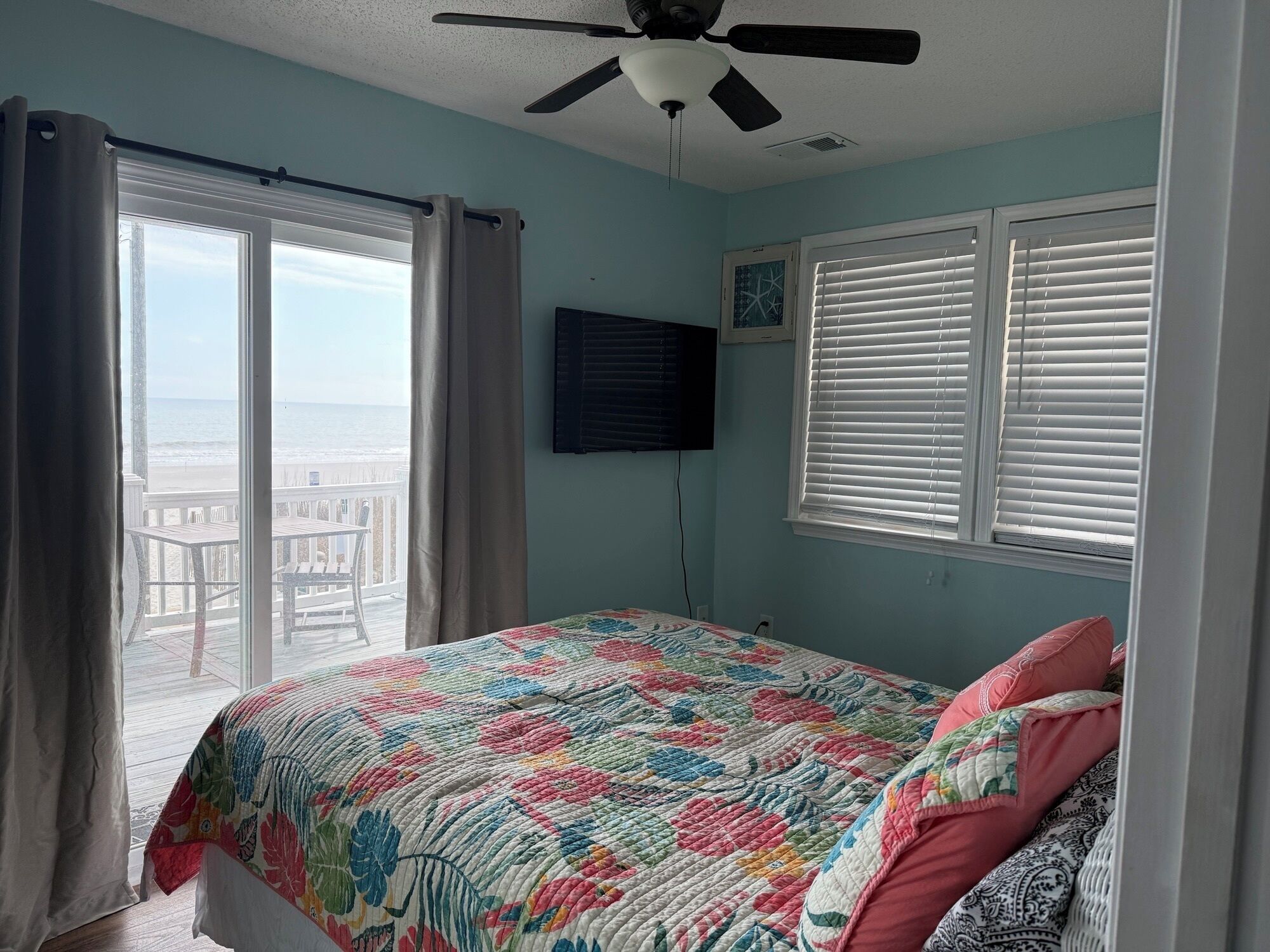 Un dormitorio con cama, ventilador de techo, televisor y vista a la playa.