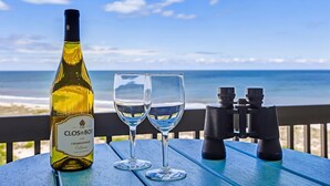Una botella de Chardonnay Clos du Bois, dos copas y unos binoculares sobre una mesa con vista al océano.