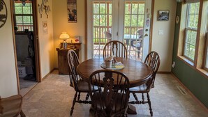 A dining area with a wooden table and chairs, a chandelier, and a view through the glass doors. - Ponderosa Cabin with Private Hot Tub - Near Mt Rushmore and Hills Attractions (Custer)