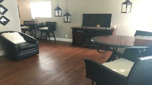 Un coin repas avec une table ronde et des chaises, un fauteuil en cuir noir, un téléviseur et des lanternes suspendues.
