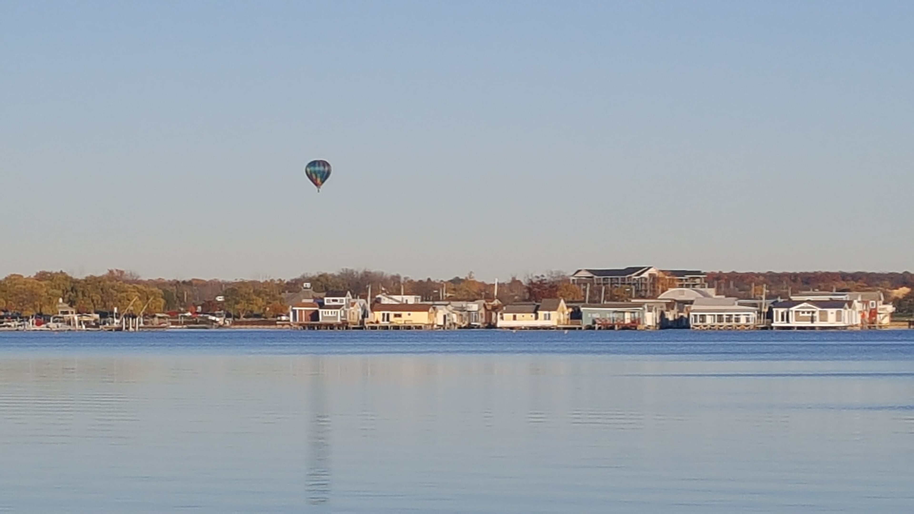 Une vue sur le bord de l’eau, avec une montgolfière dans le ciel et une rangée de maisons le long de la côte.