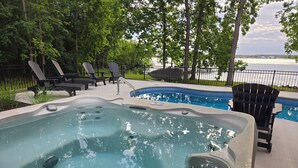 A hot tub with a view of a lake, surrounded by lounge chairs and a fence.