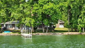 A lakeside property with a dock, a boat, and two houses surrounded by trees.