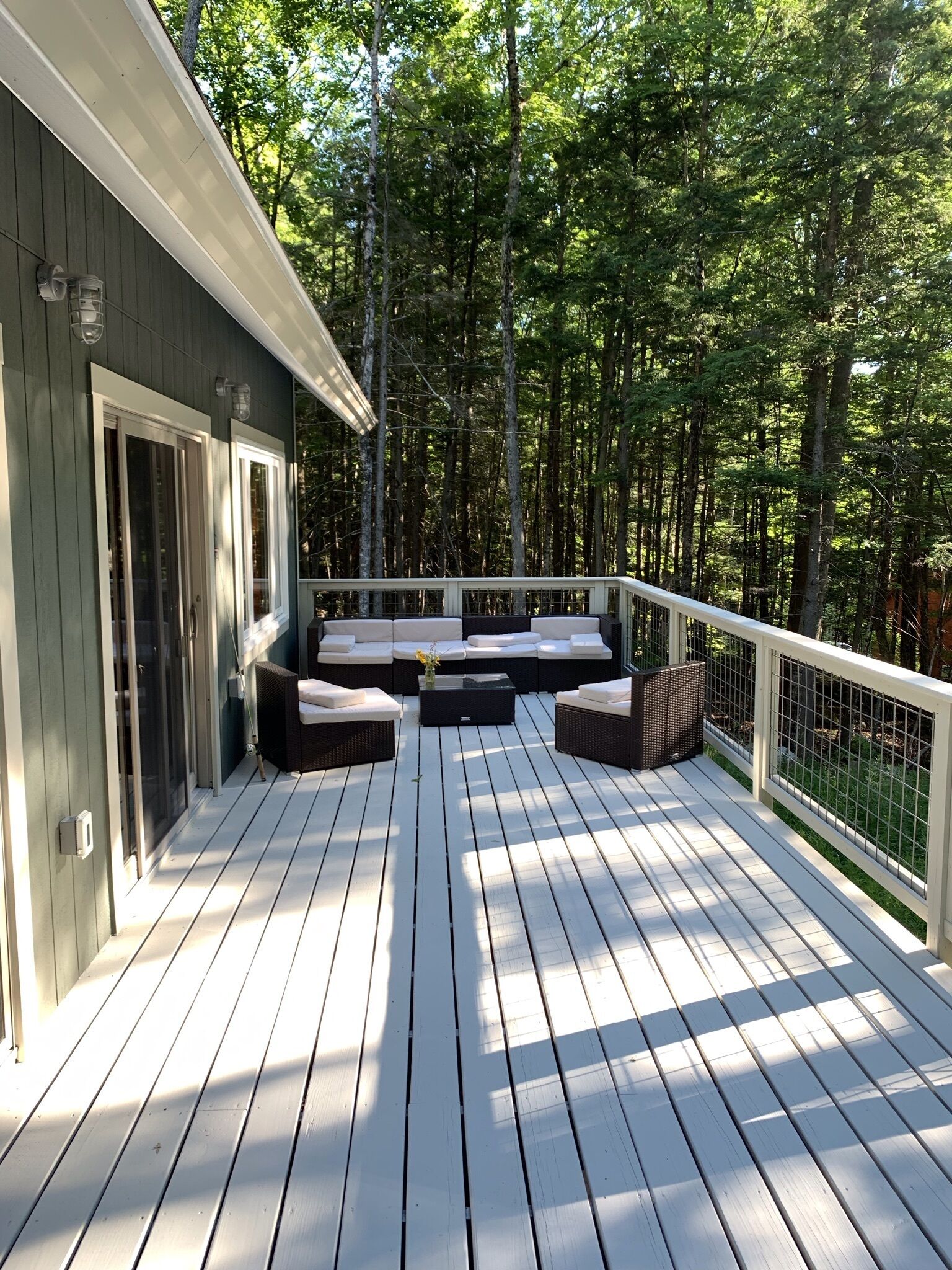 A wooden deck with outdoor seating and a railing, surrounded by trees.
