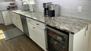 A modern kitchen with white cabinets, granite countertops, a coffee maker, and a water dispenser. - 10 Star Reviews-BEACHFRONT Home, N Cape by State Park, Elevator, Screen Porch  (Cape San Blas)