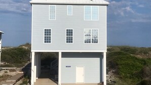 A two-story building with a garage, a covered entrance, and a clear sky. - 10 Star Reviews-BEACHFRONT Home, N Cape by State Park, Elevator, Screen Porch  (Cape San Blas)
