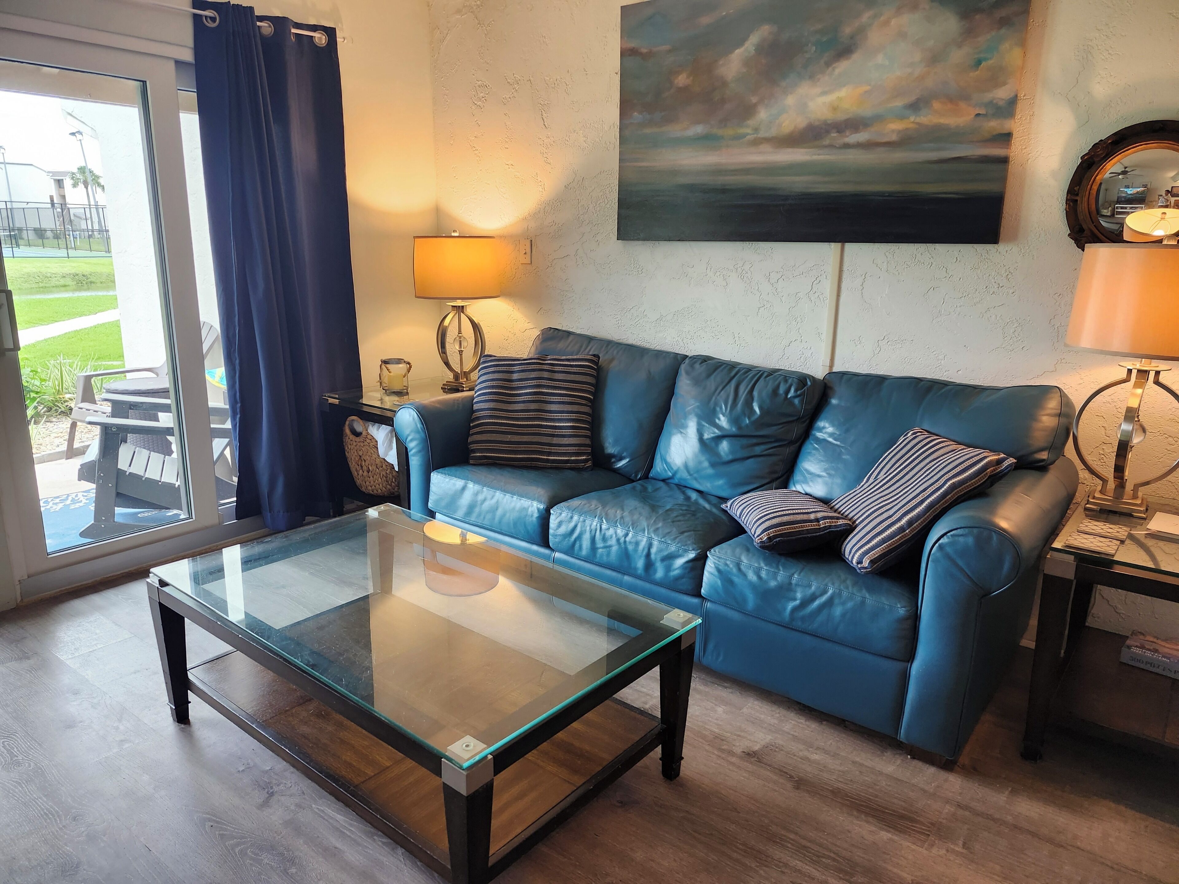 Un salon avec une table basse en verre, un canapé en cuir bleu et un tableau accroché au mur.