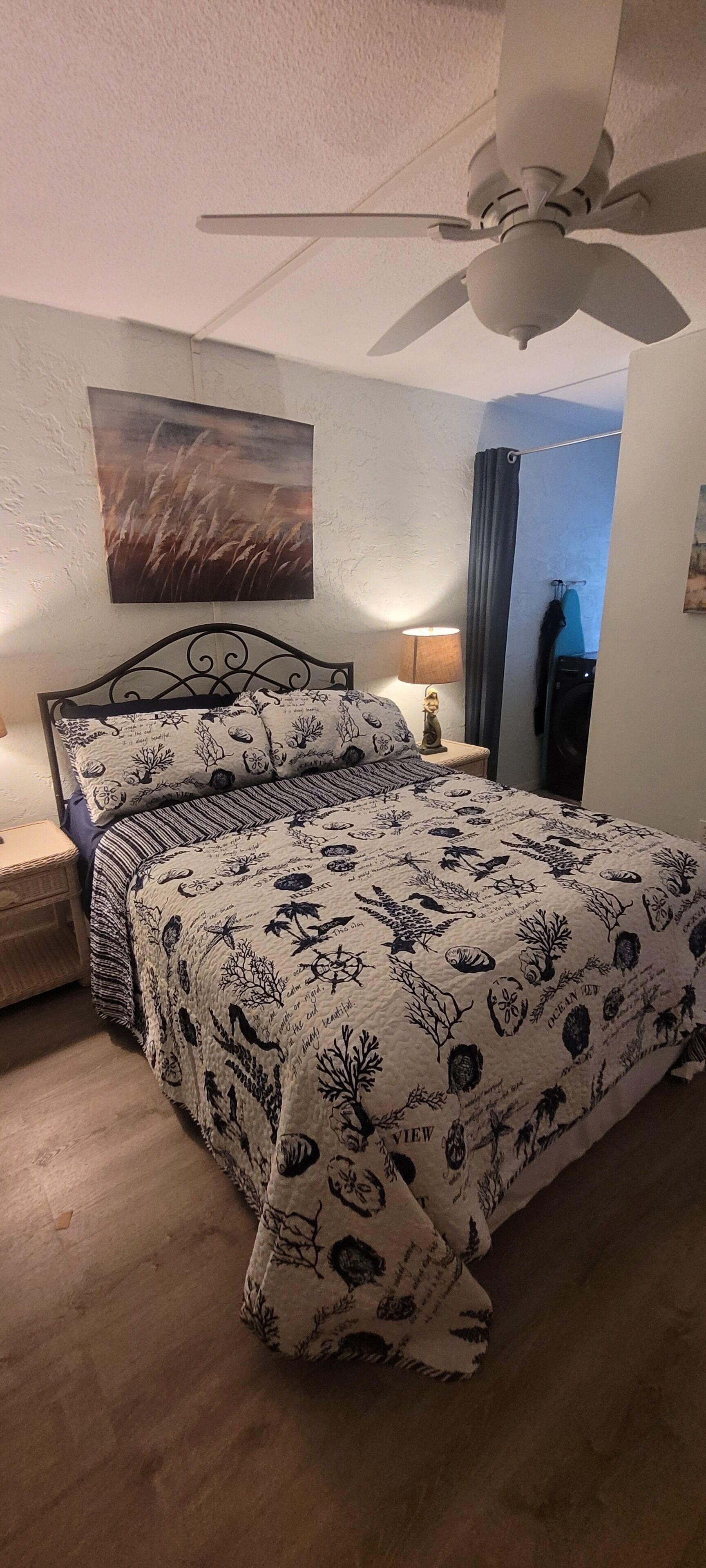 Une chambre à coucher avec un lit, un ventilateur de plafond, une table de chevet, une lampe et un tableau au mur.