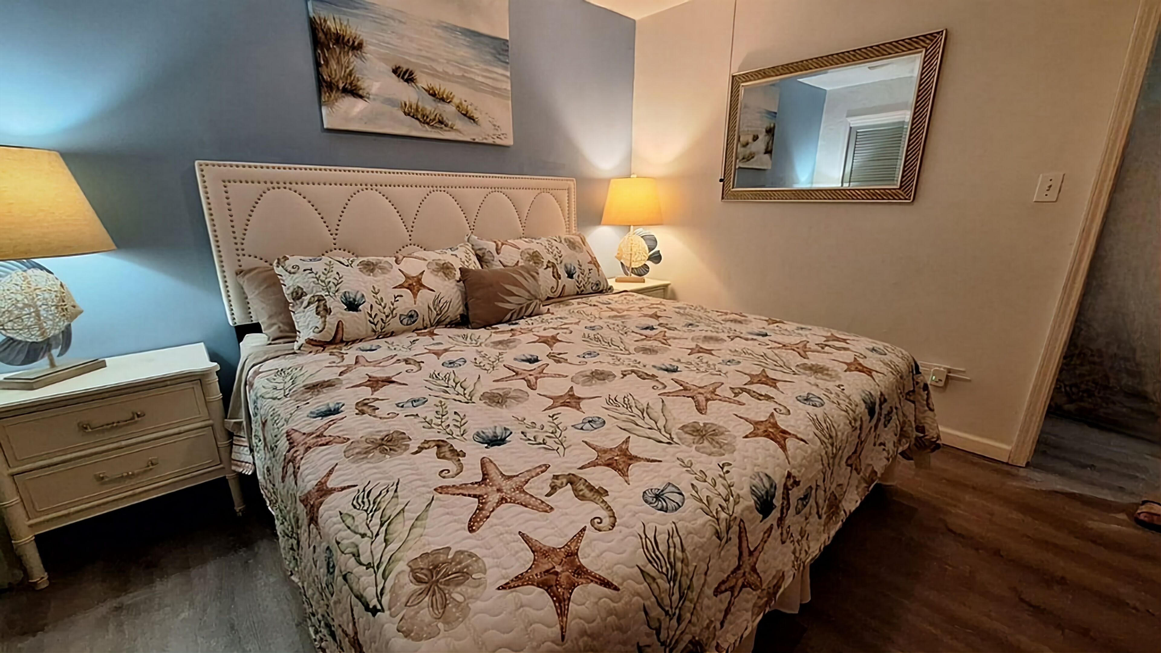 Een slaapkamer met een bed, nachtkastjes, een lamp, een spiegel en een schilderij aan de muur.