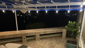 Une terrasse sur le toit avec un banc en pierre, un coin salon avec des coussins et un pot de fleurs.