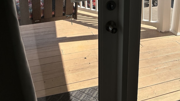 A wooden deck with a view of the beach, a sign instructing to hold onto the door during windy days, and a clear blue sky.