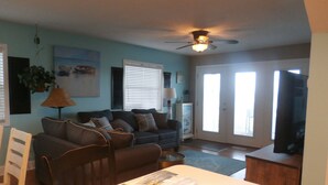 A living room with a sofa, chairs, a dining table, and a ceiling fan.