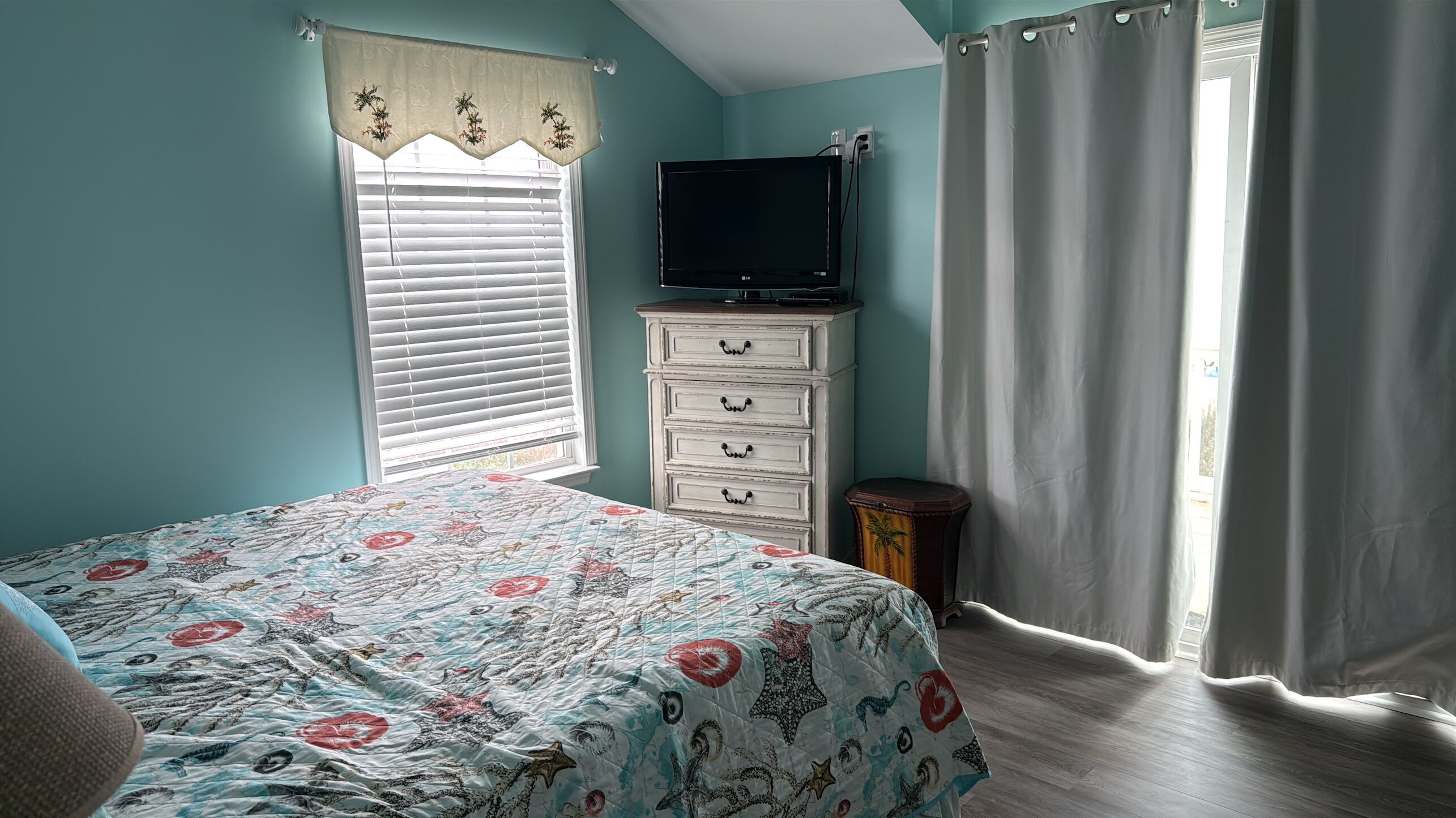 A bedroom with a bed, dresser, TV, and curtains.