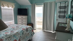 Une chambre à coucher avec un lit, une commode, une télévision et une vue sur l’océan.