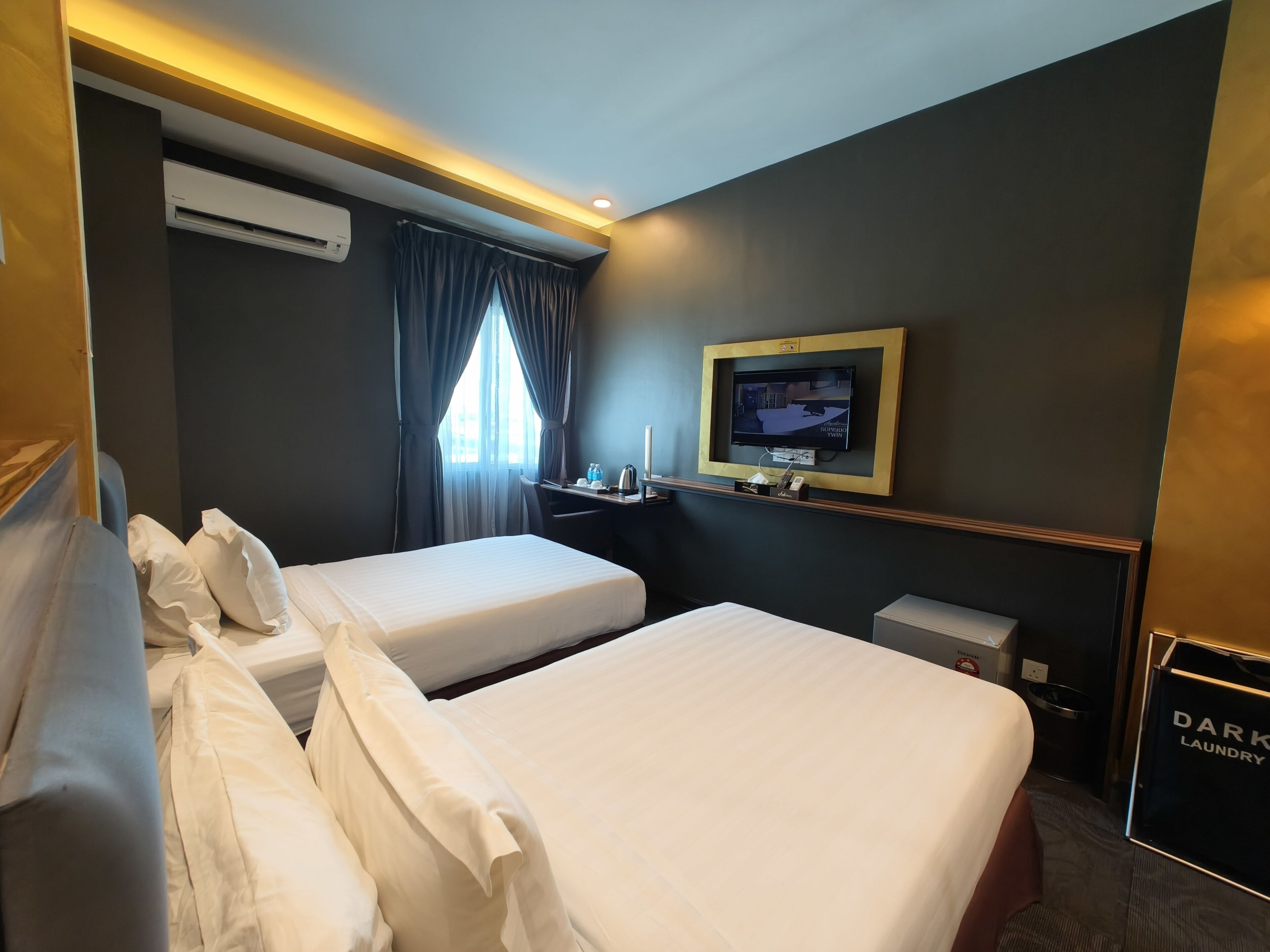 A hotel room with two beds, a TV, a desk, and a dark-colored wall.