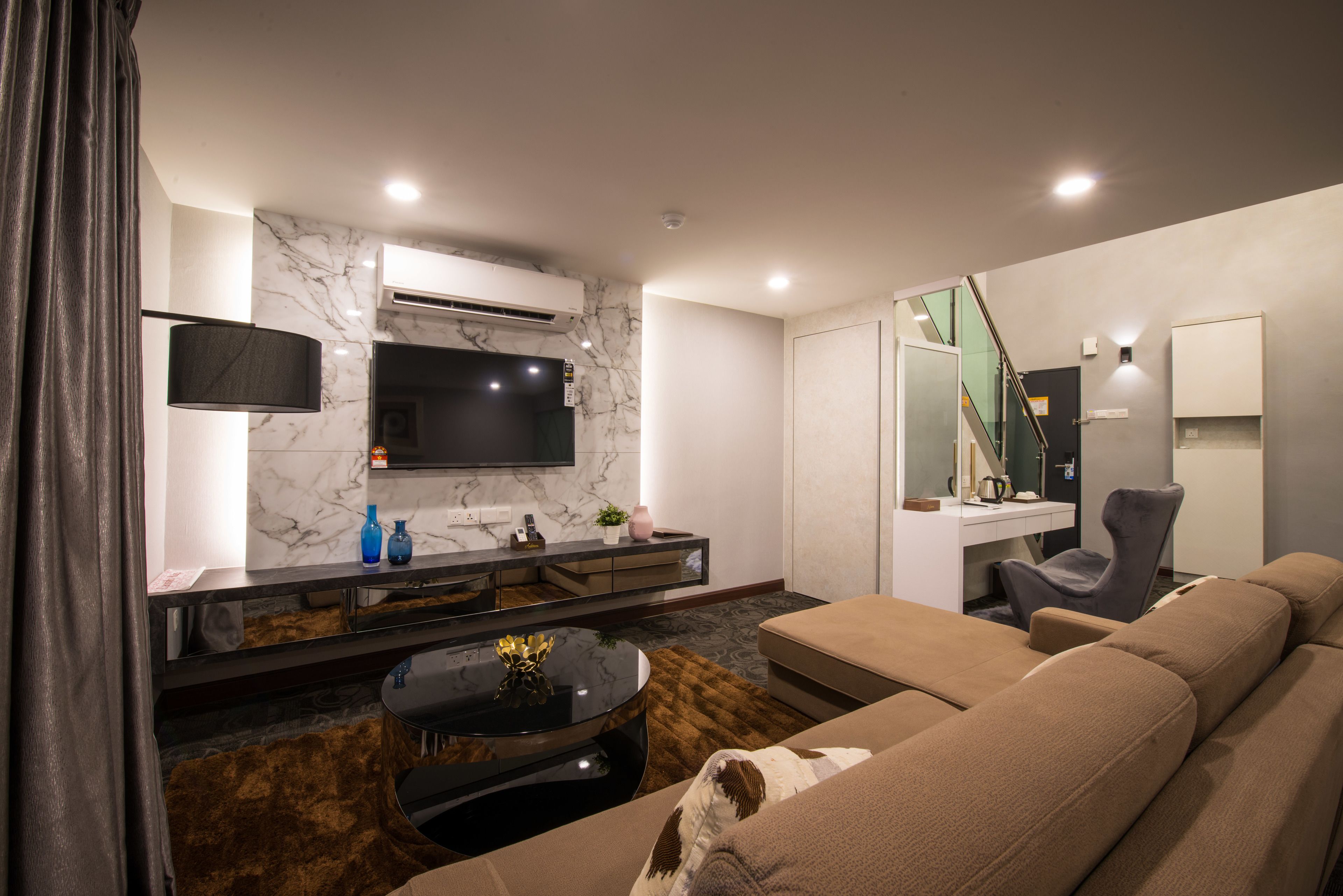 Una sala de estar moderna con un sofá, una mesa de centro, un televisor instalado en la pared y una escalera que sube a otro nivel.