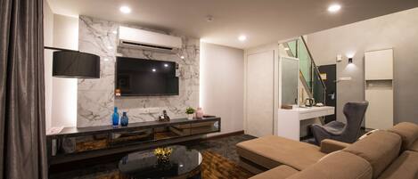 Una sala de estar moderna con un sofá, una mesa de centro, un televisor instalado en la pared y una escalera que sube a otro nivel.